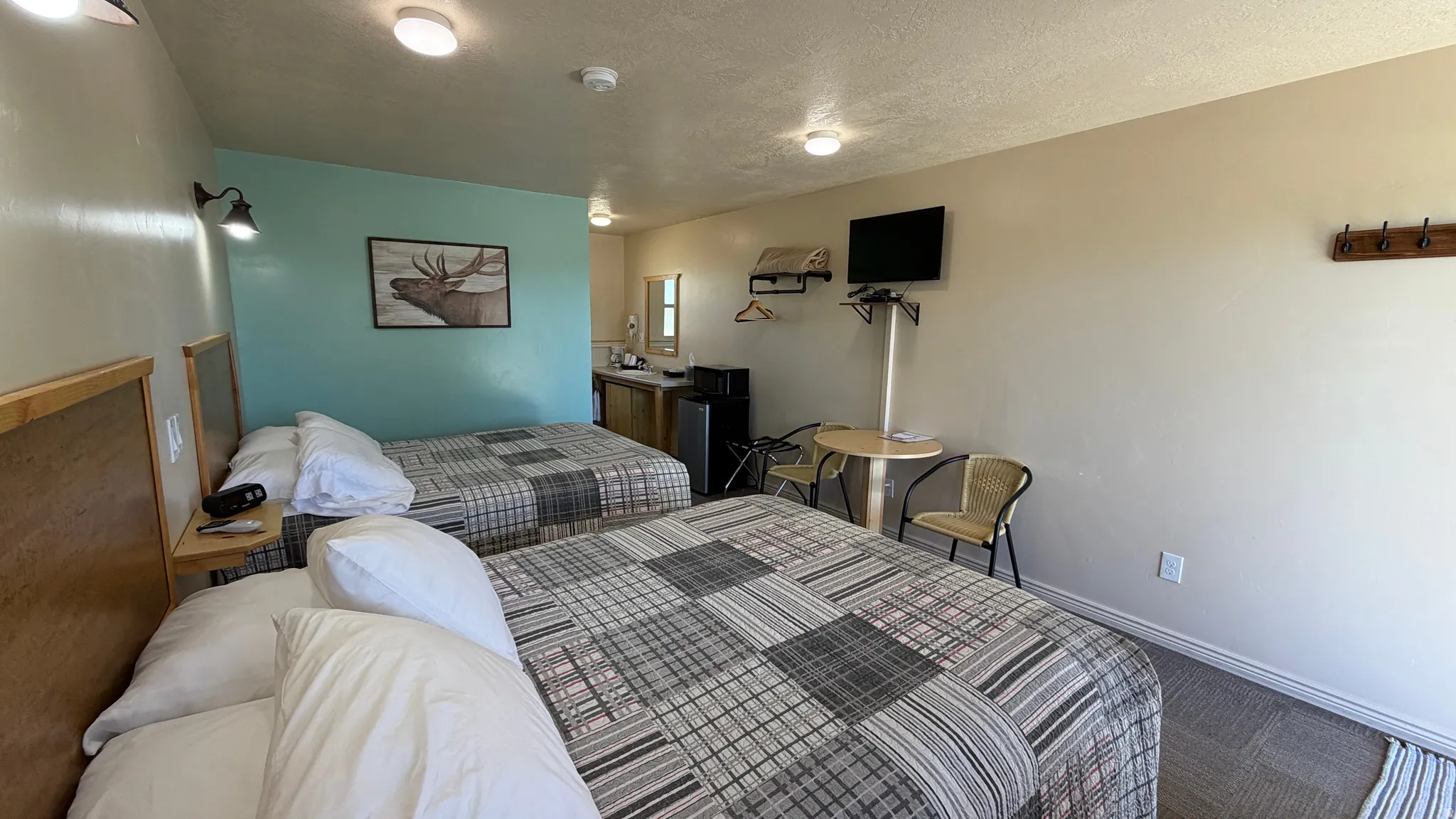 Sleeping area featuring two beds with patterned bedspreads, wood-finish headboards, a wall-mounted television, and a built-in countertop with an integrated sink and mirror