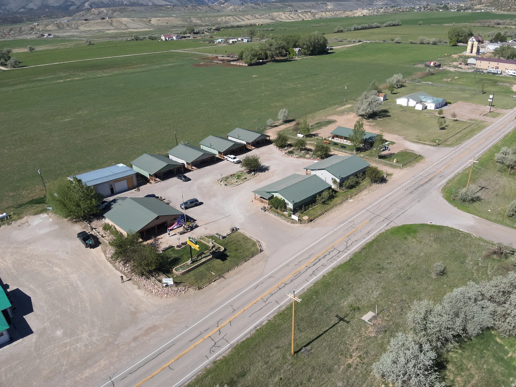 Aerial perspective showcasing multiple buildings with green metal roofs, extensive gravel parking areas, and adjacent green fields