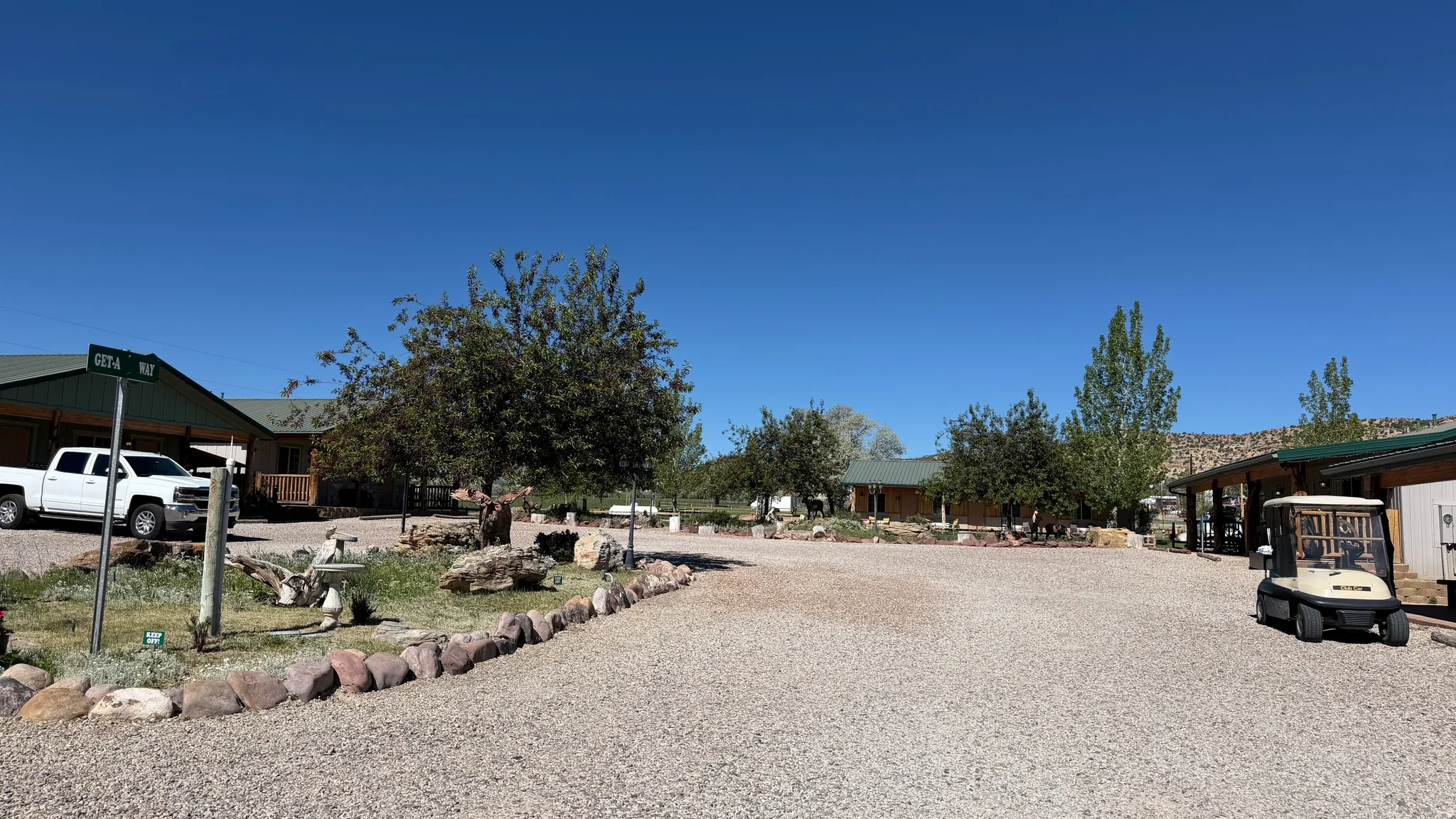 Gravel driveway with a stone border leading to multiple structures, including a single-story building with a covered porch and a prominent green roof