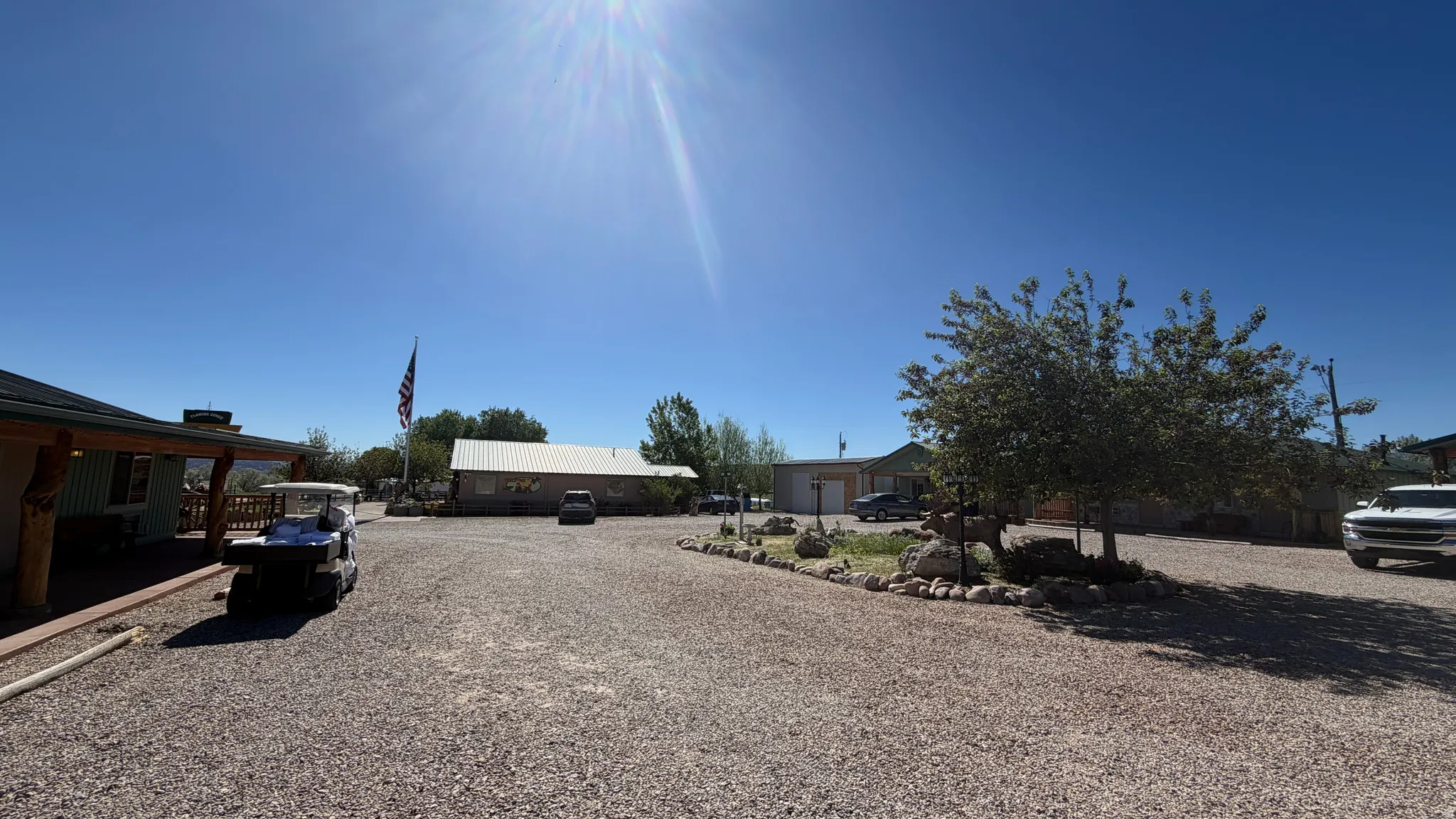 Expansive gravel driveway providing ample parking, bordered by mature trees and natural rock landscaping