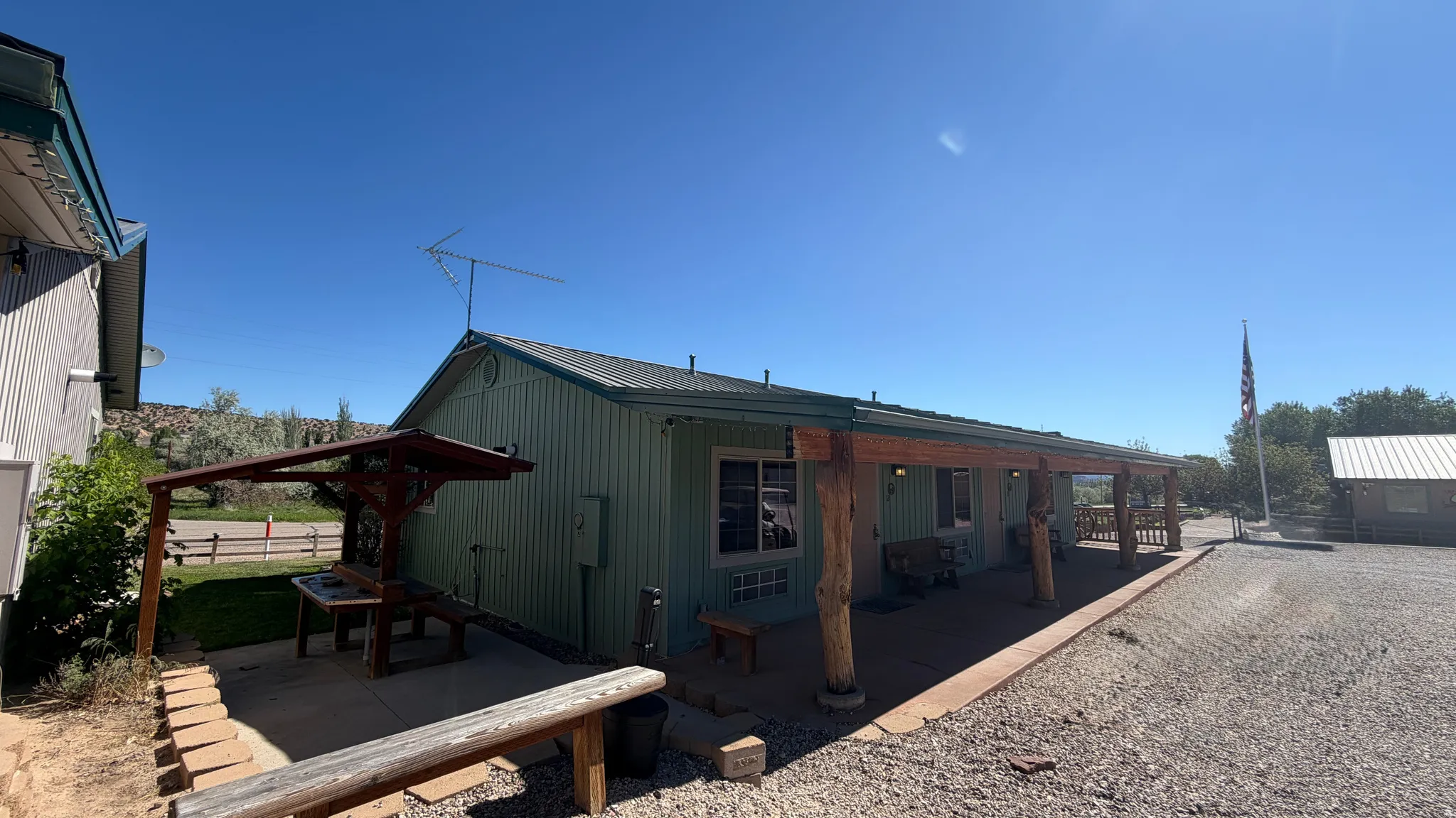 Mint green siding structure featuring a covered porch with rustic wood posts, a metal roof, and window-mounted air conditioning units
