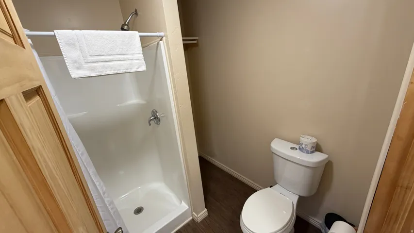Bathroom featuring a white shower stall with chrome fixtures, a white toilet, wood-finish flooring, and light-toned wall paint