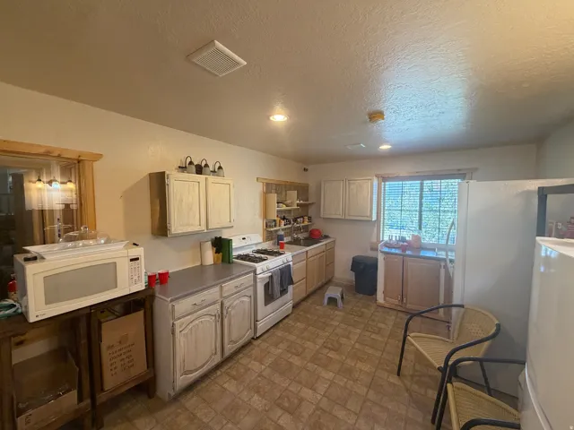 Kitchen featuring a gas range, white cabinetry, and textured ceiling