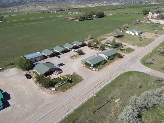 Aerial perspective showcasing multiple buildings with green metal roofs, extensive gravel parking areas, and adjacent green fields