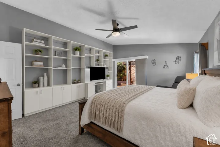 Expansive bedroom featuring a full-wall built-in shelving unit with lower cabinetry, a ceiling fan, and newer carpet with memory foam pad