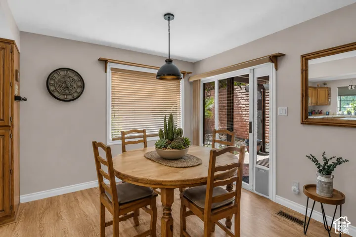 Dining area featuring wood-finish flooring, a pendant light fixture, a window with horizontal blinds, and a sliding glass door with vertical blinds