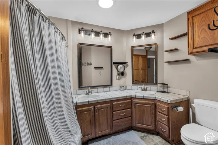 Bathroom featuring a dual vanity with wood cabinetry, tile countertops, two undermount sinks, jetted tub