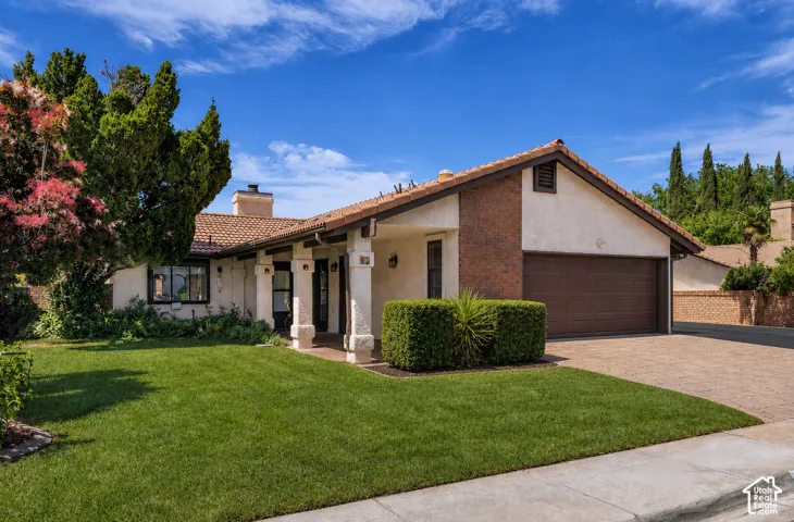 Stucco exterior with brick accents, terracotta tile roof, attached garage, paved driveway, and established landscaping