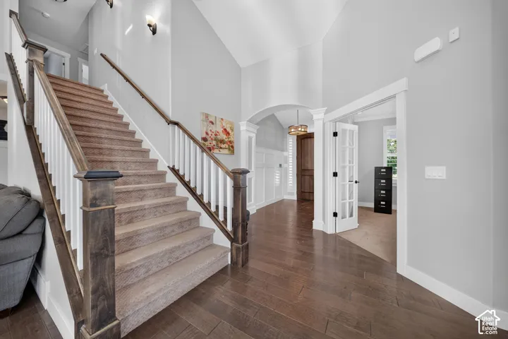 Welcoming foyer showcasing soaring ceilings, wood-finish stair treads with white railings and wood-tone handrails, dark hardwood flooring, and abundant natural light.