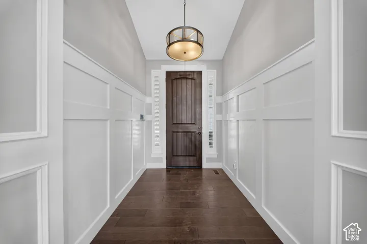Elegant hallway showcasing crisp white wainscoting and panel-molded walls, rich dark wood-finish flooring, and a coordinating pendant light fixture suspended from the ceiling