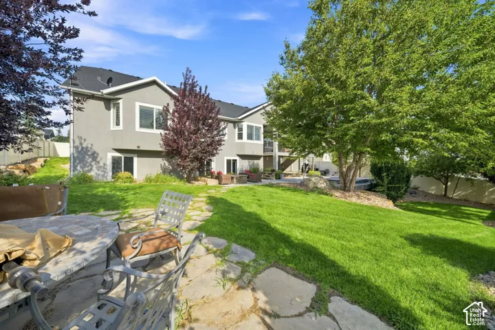 Expansive backyard featuring a stone patio, manicured lawn, mature trees, and a terraced landscape