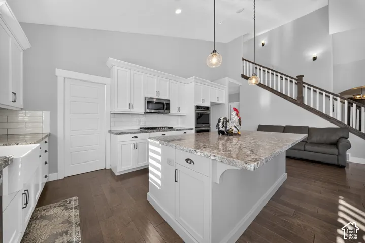 Gourmet kitchen featuring white shaker cabinetry, stainless steel appliances, and a large center island with stone countertops