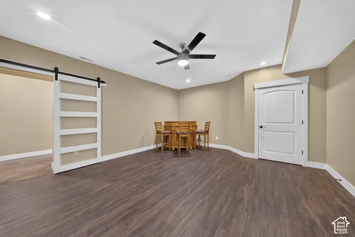 Spacious room featuring wood-finish flooring, a ceiling fan with integrated lighting, and white sliding barn door with horizontal slat detailing