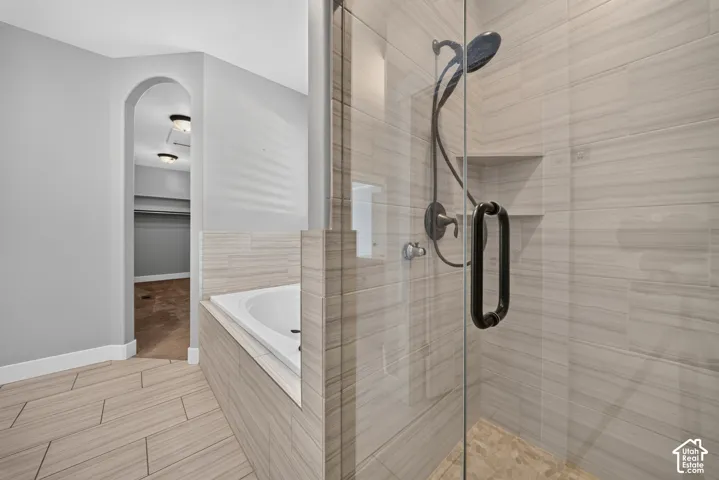 Spa-inspired primary bathroom featuring a walk-in shower with frameless glass enclosure, dual showerheads with bronze fixtures, and linear wood-finish tile walls