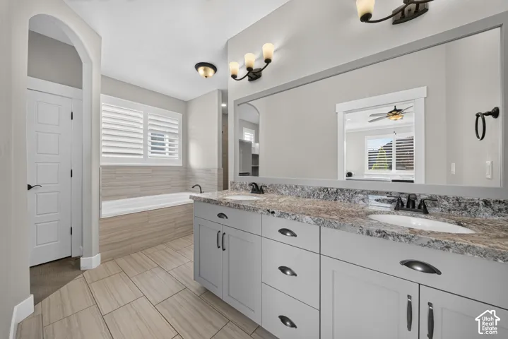 Primary Bathroom featuring dual vanities with ample storage, granite countertops, brushed nickel hardware, and a large framed mirror
