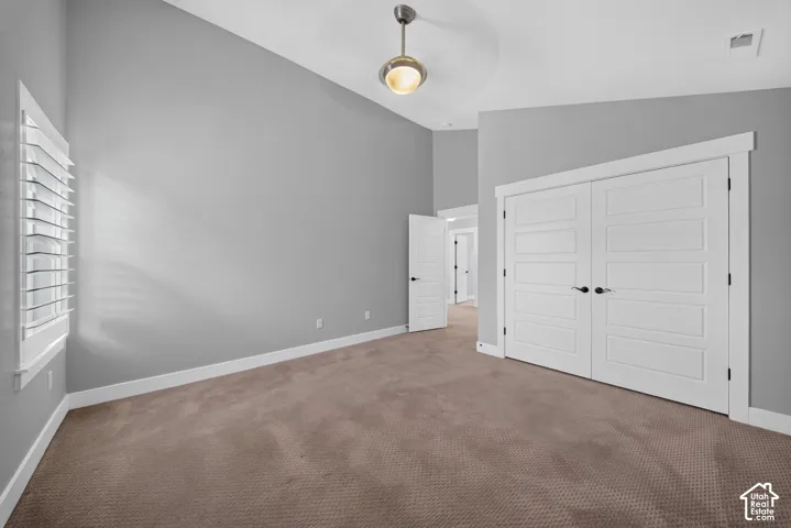 Spacious bedroom offering neutral gray walls, warm wood-finish flooring, and abundant natural light from louvered shutters