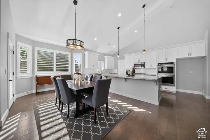 Open-concept kitchen and dining area featuring white cabinetry, stainless steel appliances, white quartz countertops, pendant lighting, and hardwood flooring throughout