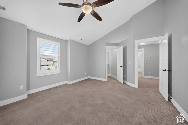 Carpeted flooring, vaulted ceiling, white interior doors, and a ceiling fan with light fixture