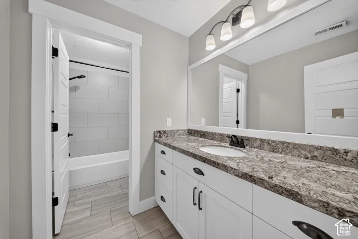 White vanity with dark hardware, stone-finish countertop, and a large mirror