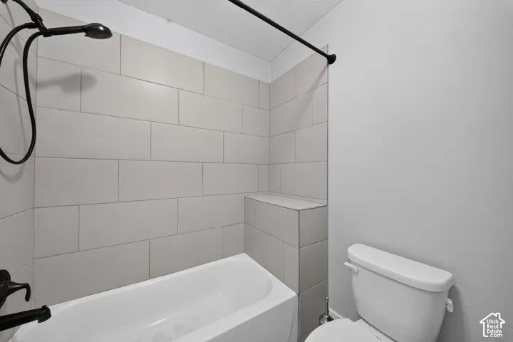 Clean, updated bathroom featuring subway tile walls, a soaking tub with integrated surround, a separate toilet, and black metal fixtures