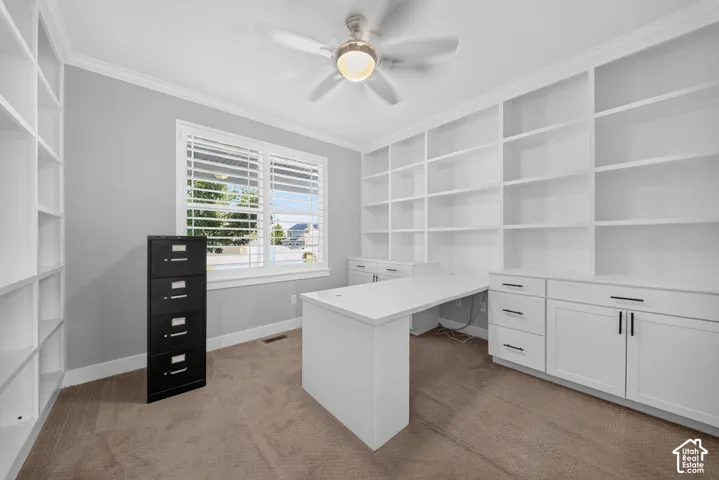 Built-in shelving and cabinetry, ceiling fan, window with plantation shutters, integrated desk, and carpeted flooring
