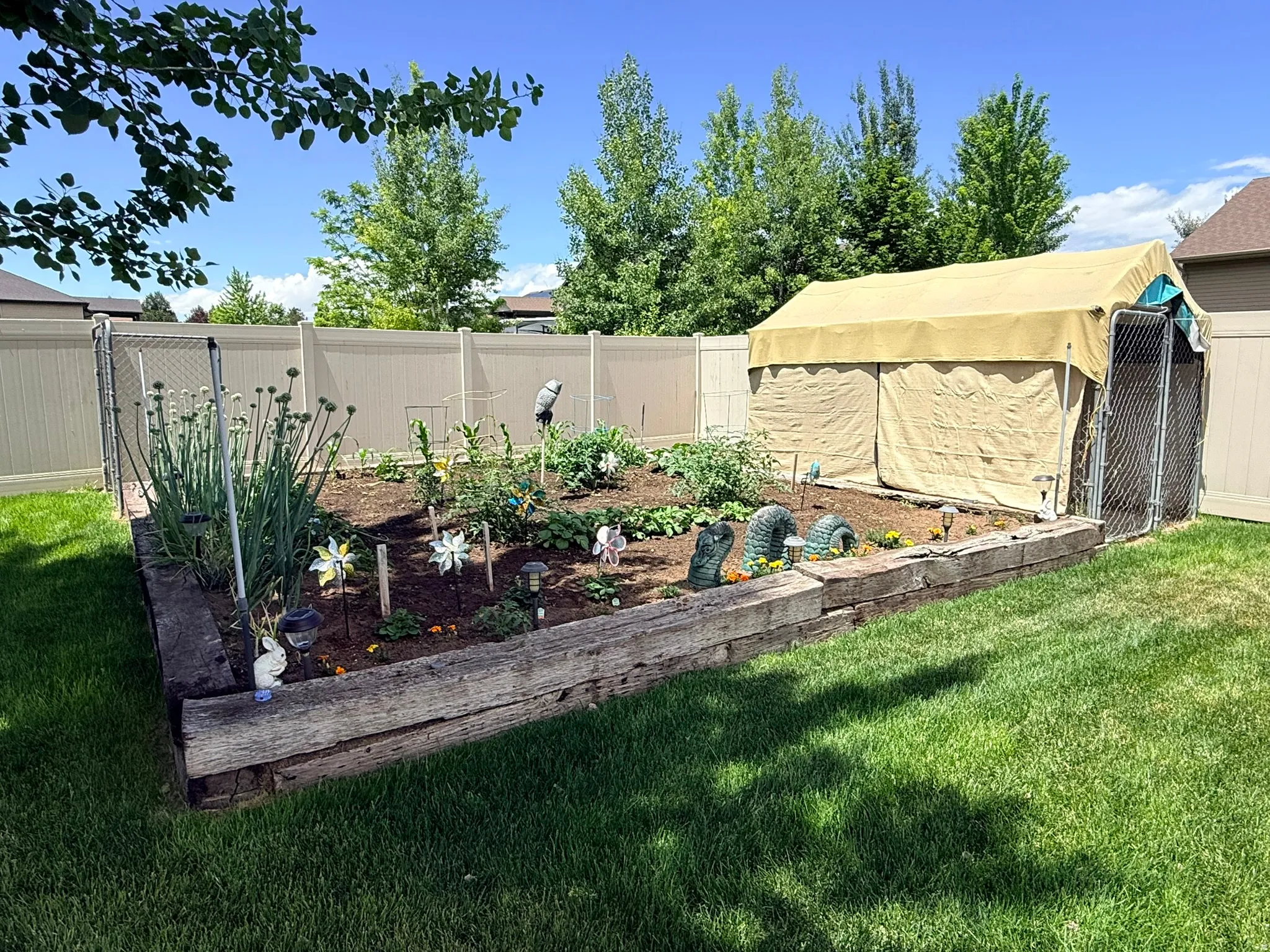 Raised garden bed with wood beam edging, cultivated planting area, and adjacent covered enclosure