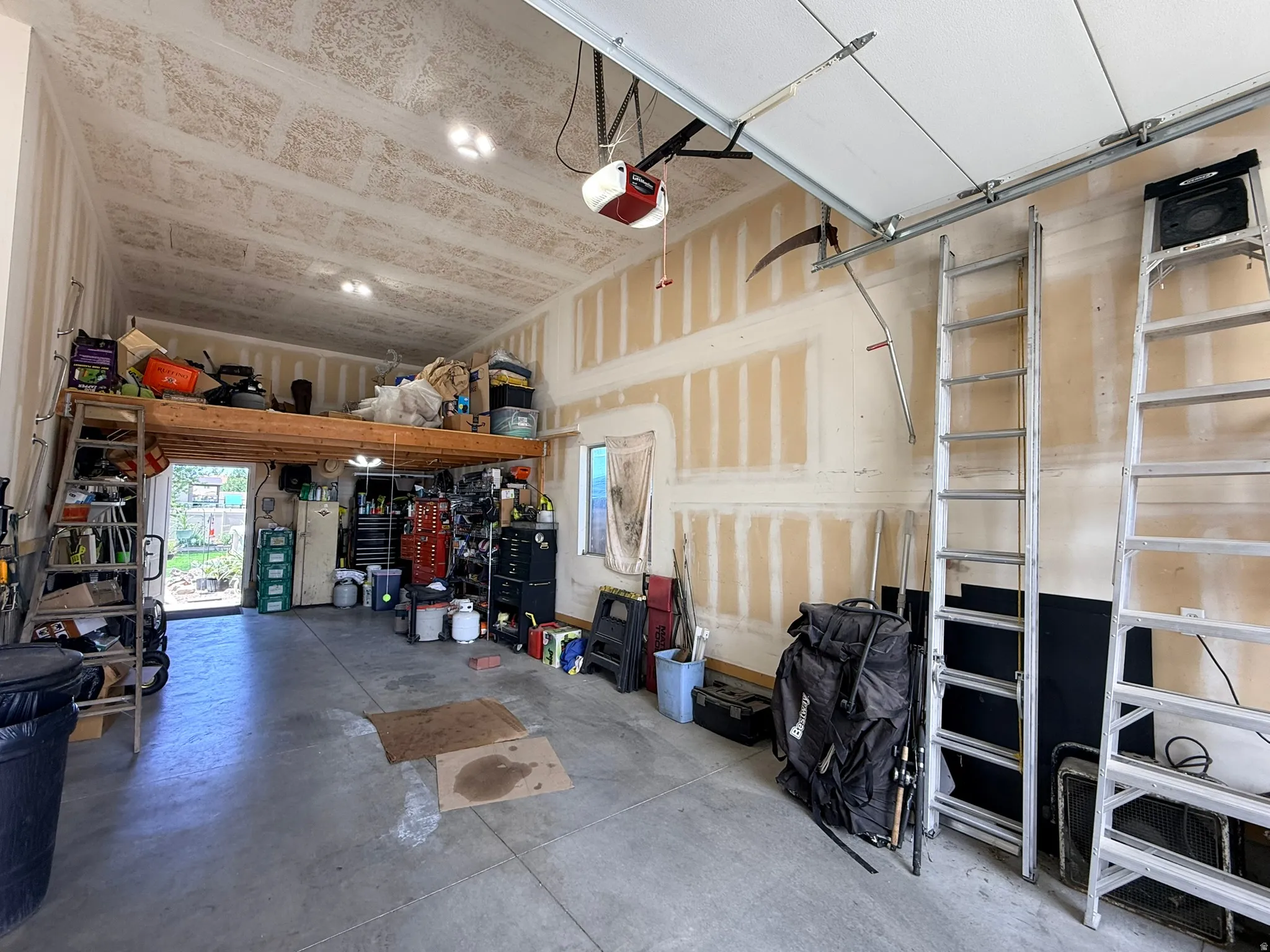 Spacious garage featuring a concrete floor, high vaulted ceiling with exposed OSB, and an integrated overhead storage loft