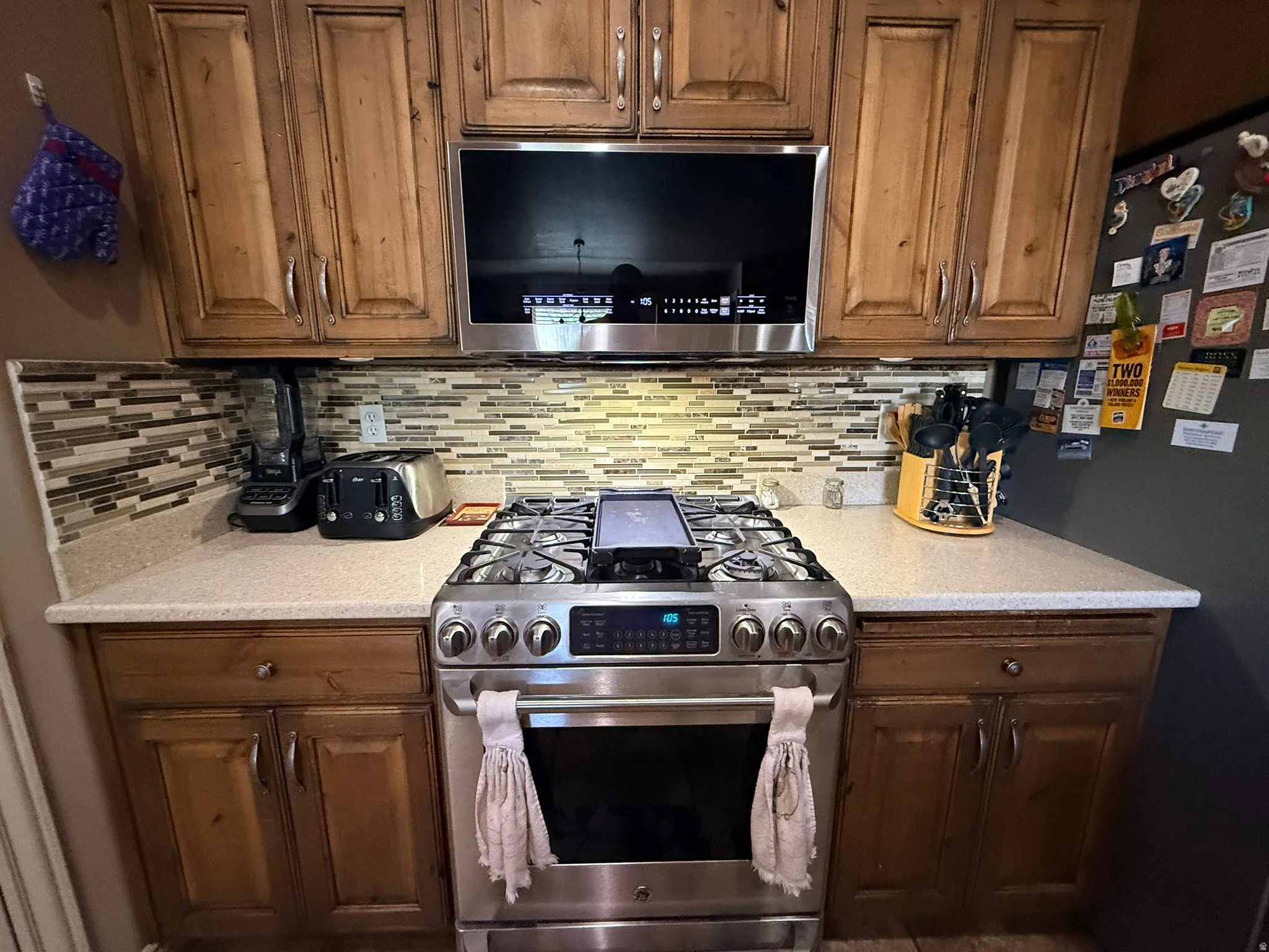 Stainless steel gas range with coordinating overhead microwave, set against a mosaic tile backsplash