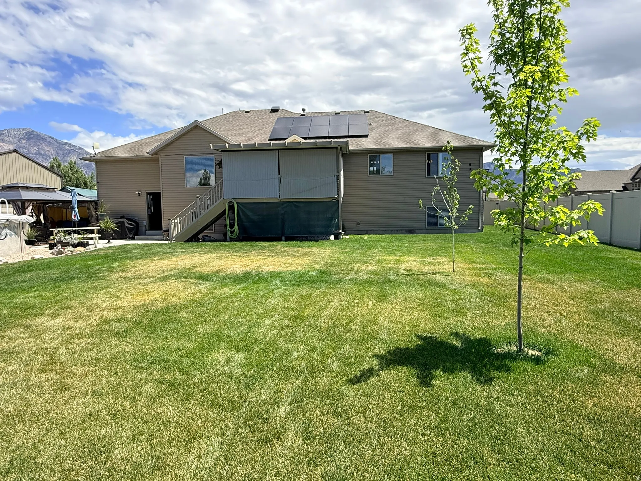 Spacious backyard featuring a large lawn, mature trees, and a multi-level deck with integrated solar panels on the roof