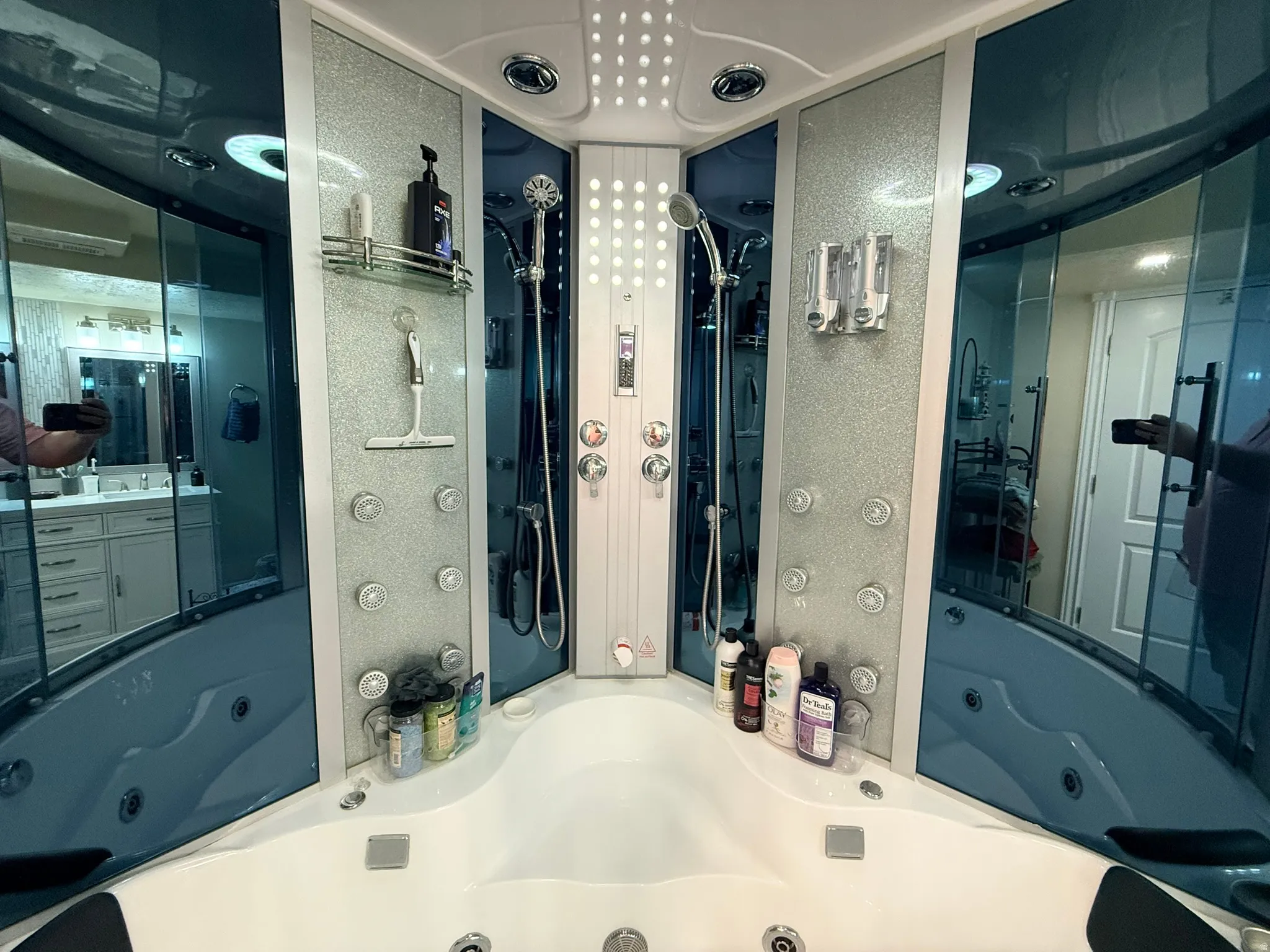 Integrated shower and jetted tub system featuring multiple body sprayers, a handheld shower fixture, and overhead lighting