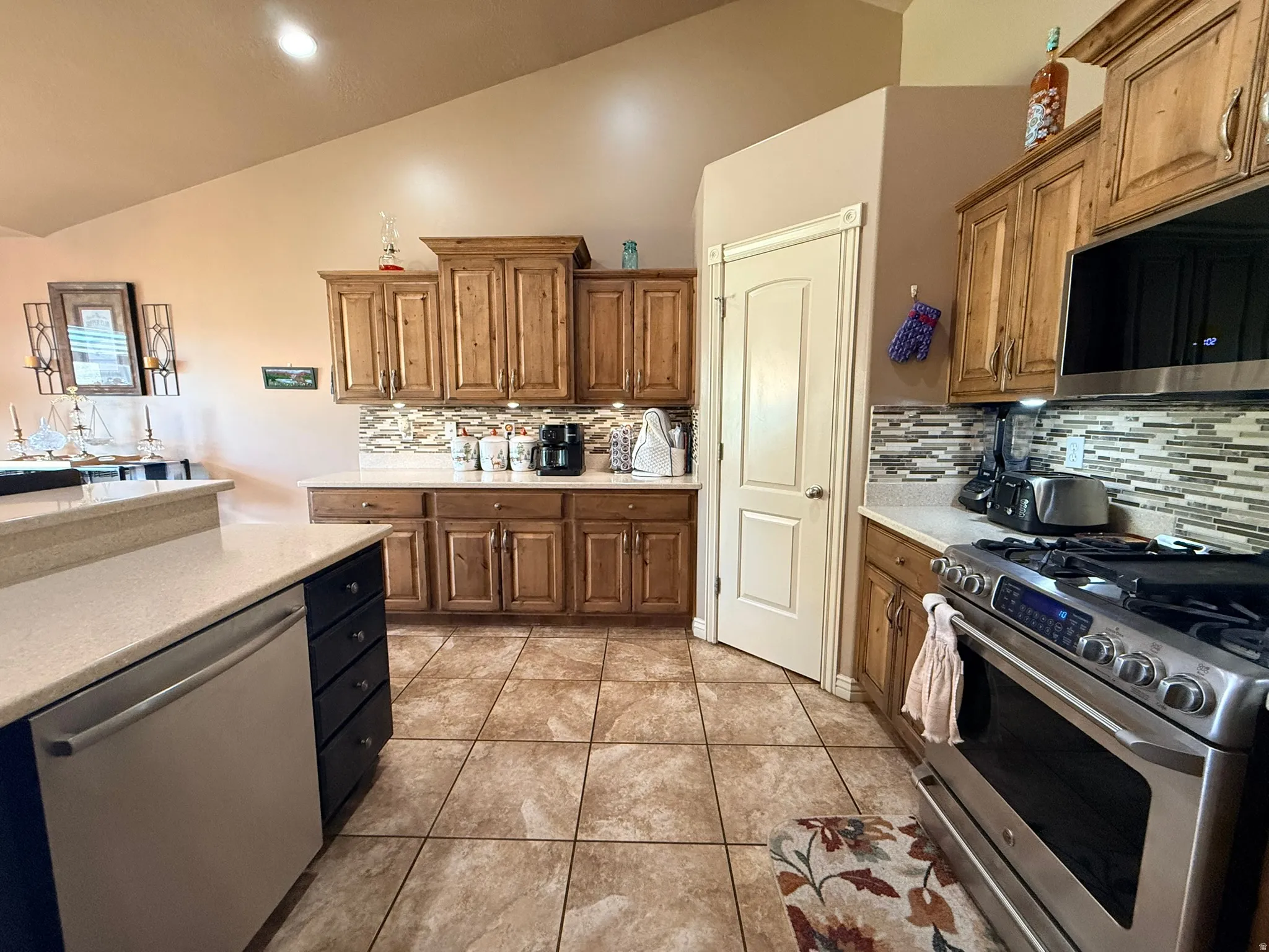 Kitchen featuring vaulted ceilings, wood cabinetry, stone countertops, a tile backsplash, and stainless steel appliances