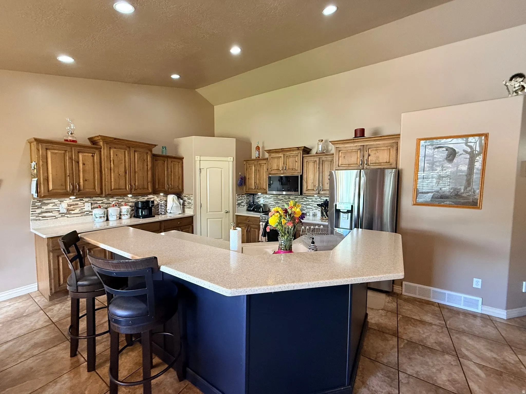 Kitchen featuring wood cabinetry, stone-look countertops, a multi-tone tile backsplash, stainless steel appliances, and recessed lighting