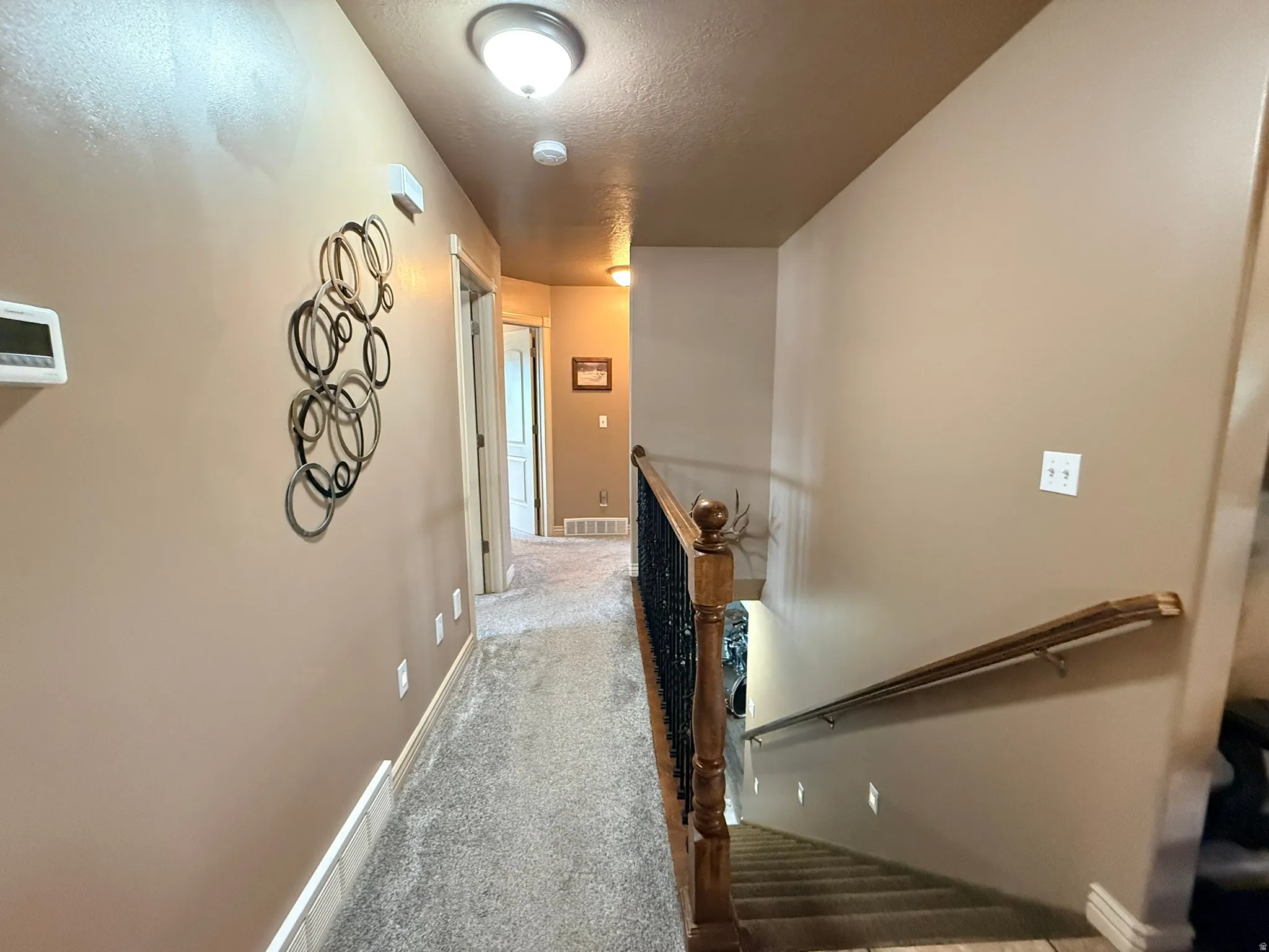 Carpeted hallway featuring a staircase with wood-finish handrails and wrought iron balusters