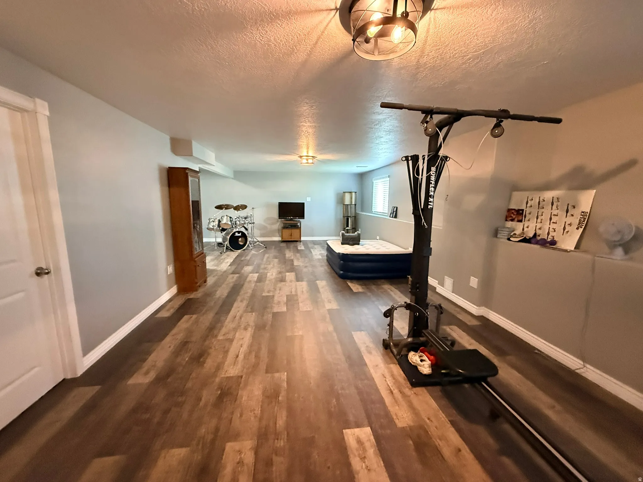 Spacious lower-level room featuring wood-finish flooring, light gray walls, and white trim