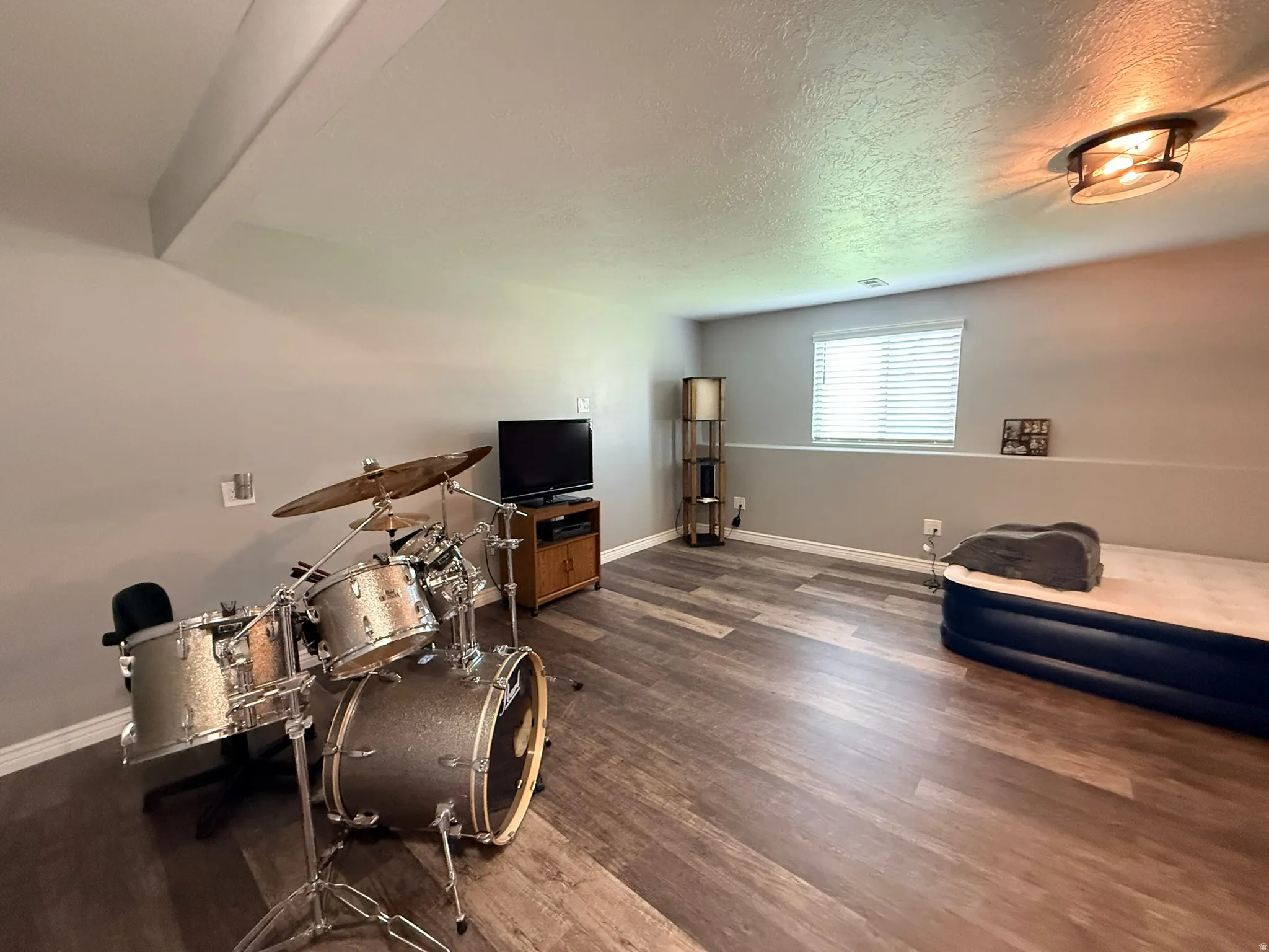 Spacious room featuring wood-finish flooring, neutral-toned walls, and a recessed window with blinds