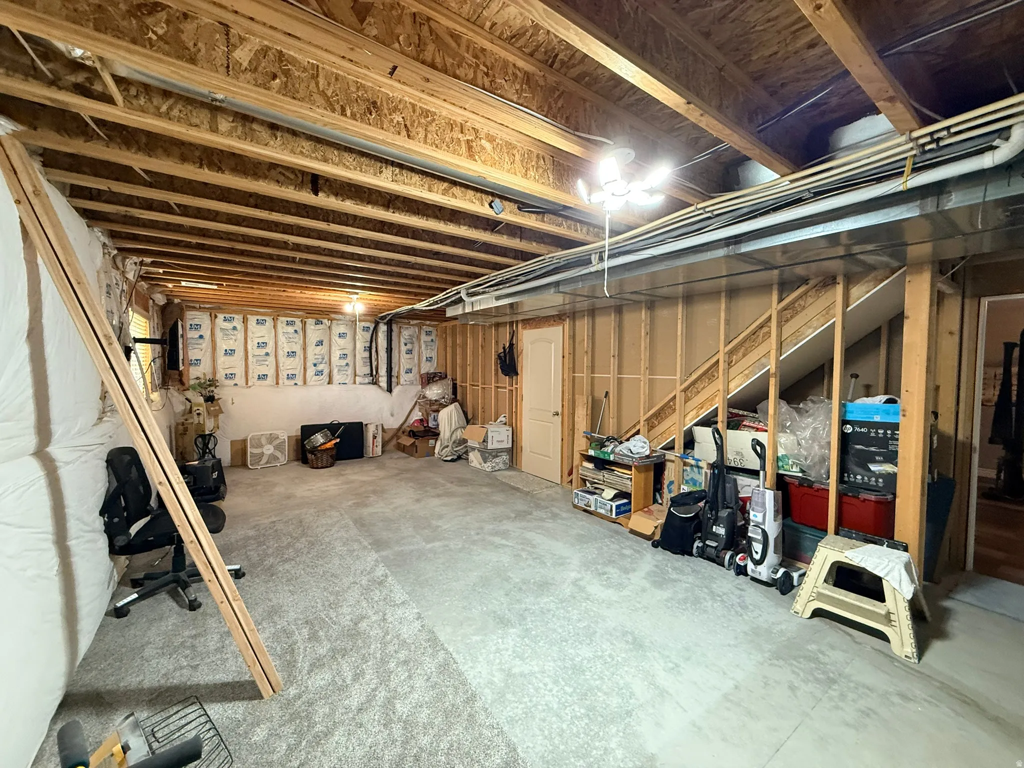 Unfinished basement offering substantial potential for customization, featuring exposed ceiling joists and framing, insulated perimeter walls, and a dedicated storage area beneath the staircase
