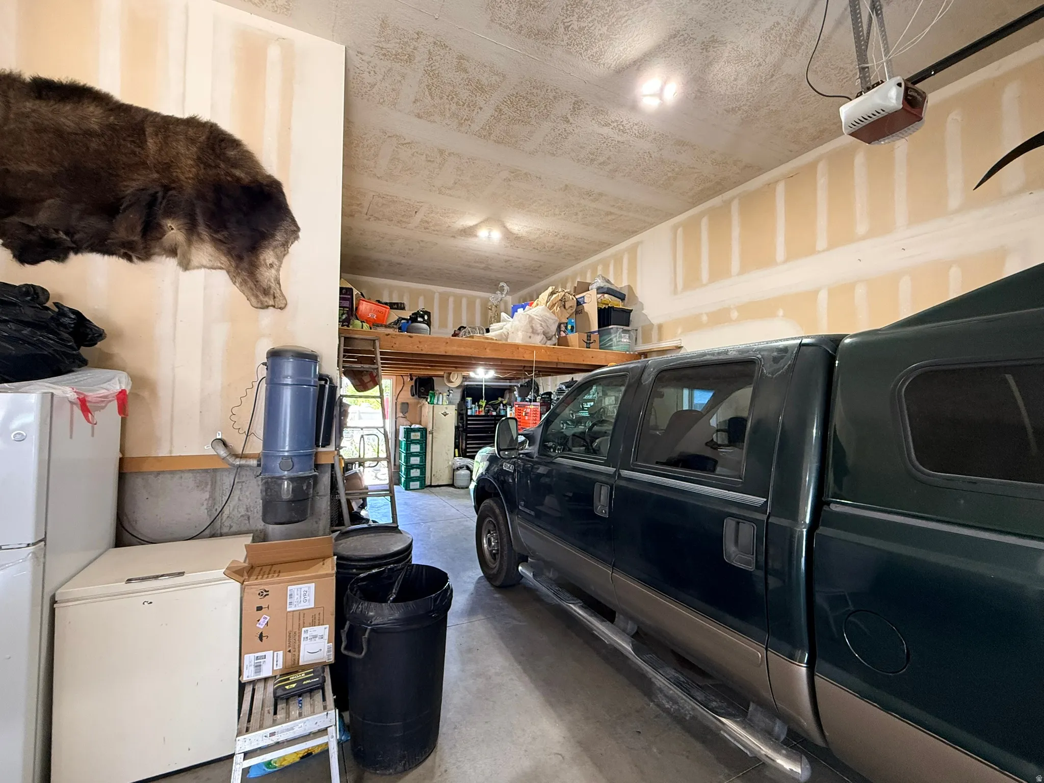 Spacious garage featuring a high ceiling, exposed wall studs, and overhead storage loft