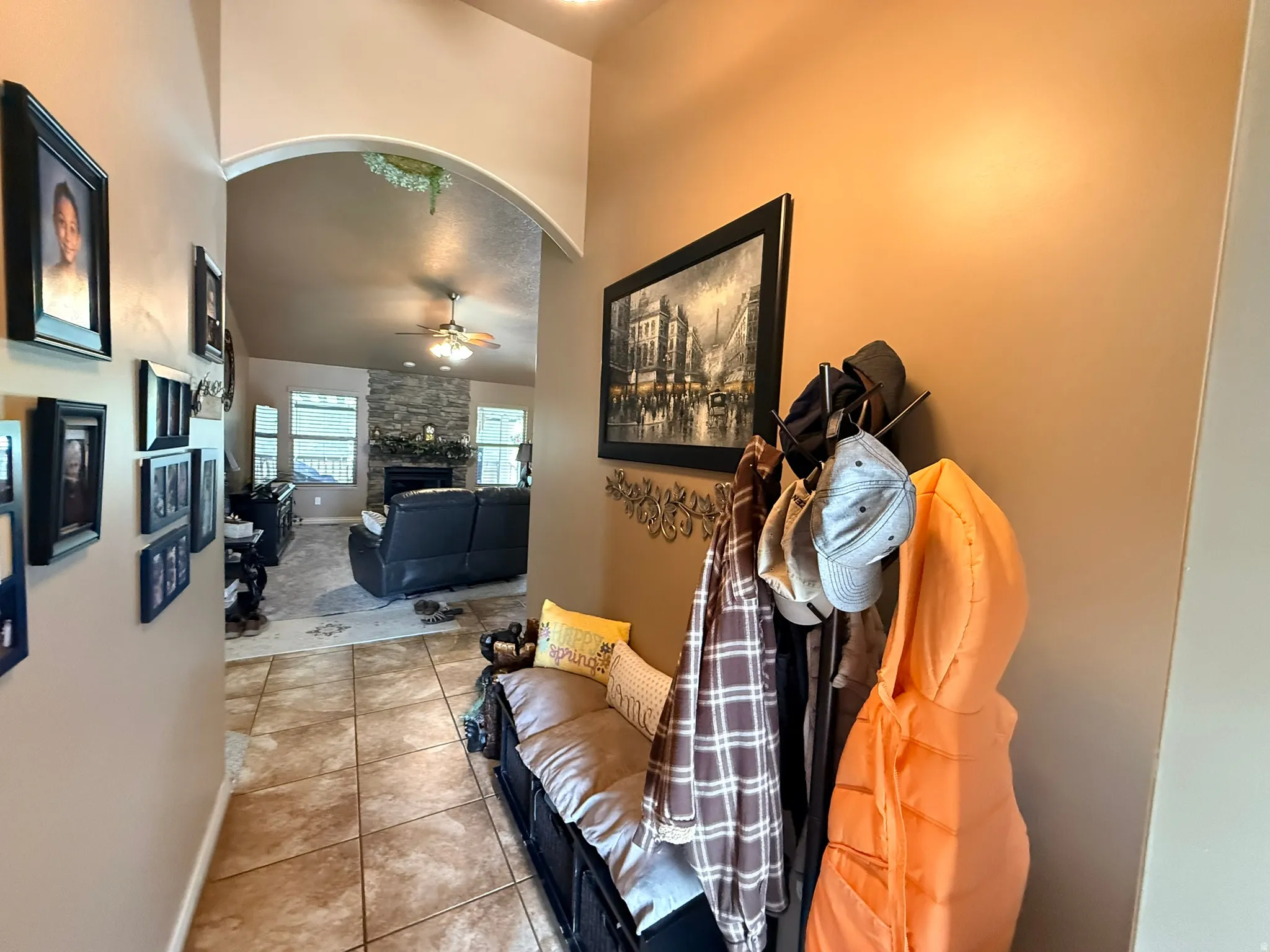 Tiled entry hallway with an arched doorway opening into a living space featuring a stone-clad fireplace and a ceiling fan