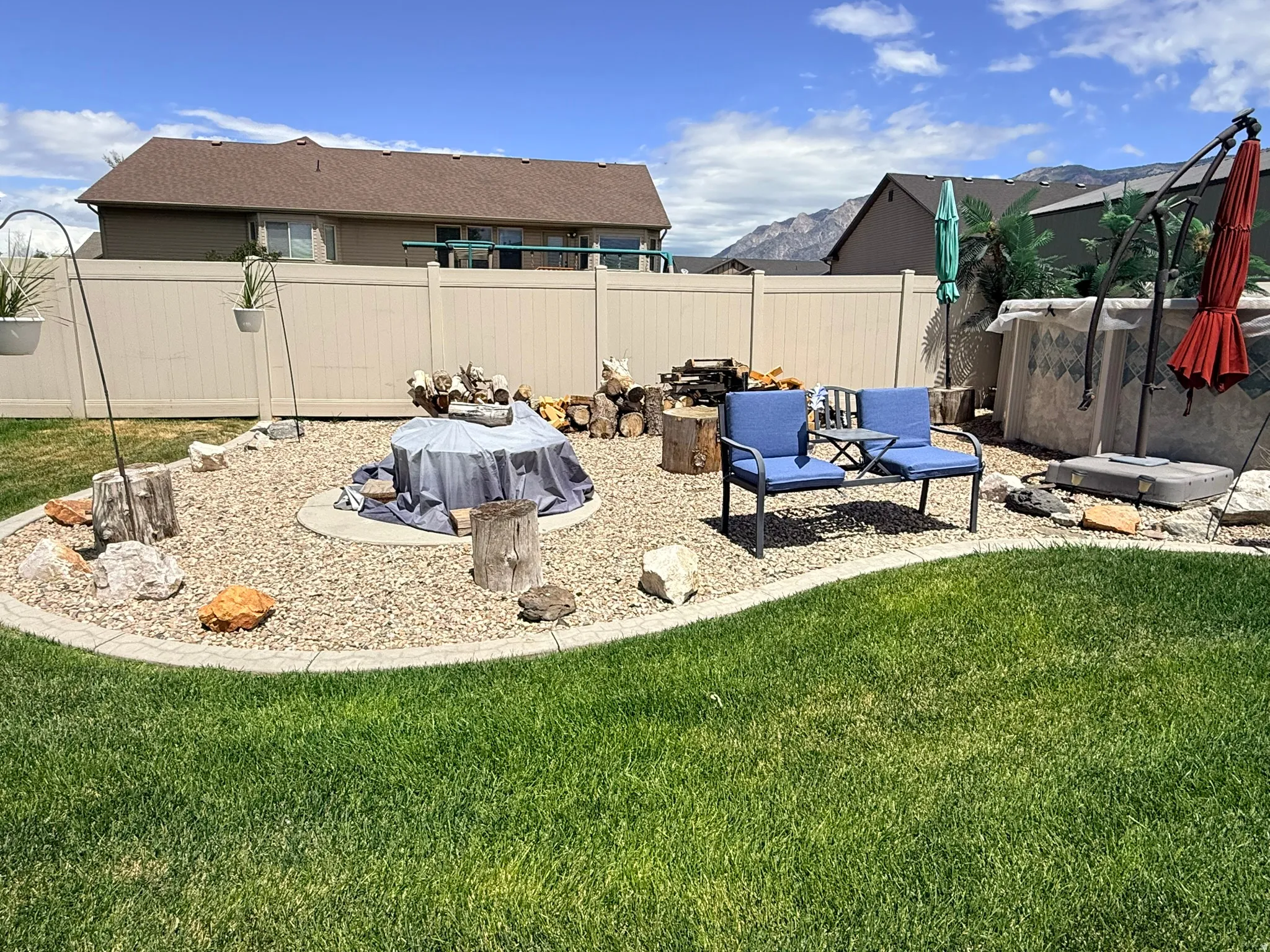 Expansive backyard featuring a manicured lawn, a gravel fire pit area with log stumps, and a privacy fence