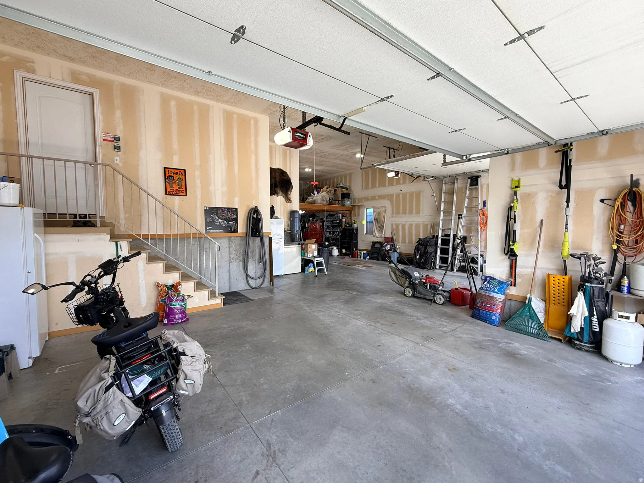 Spacious garage featuring a concrete floor, overhead garage doors, an interior staircase with metal railing, and an interior door