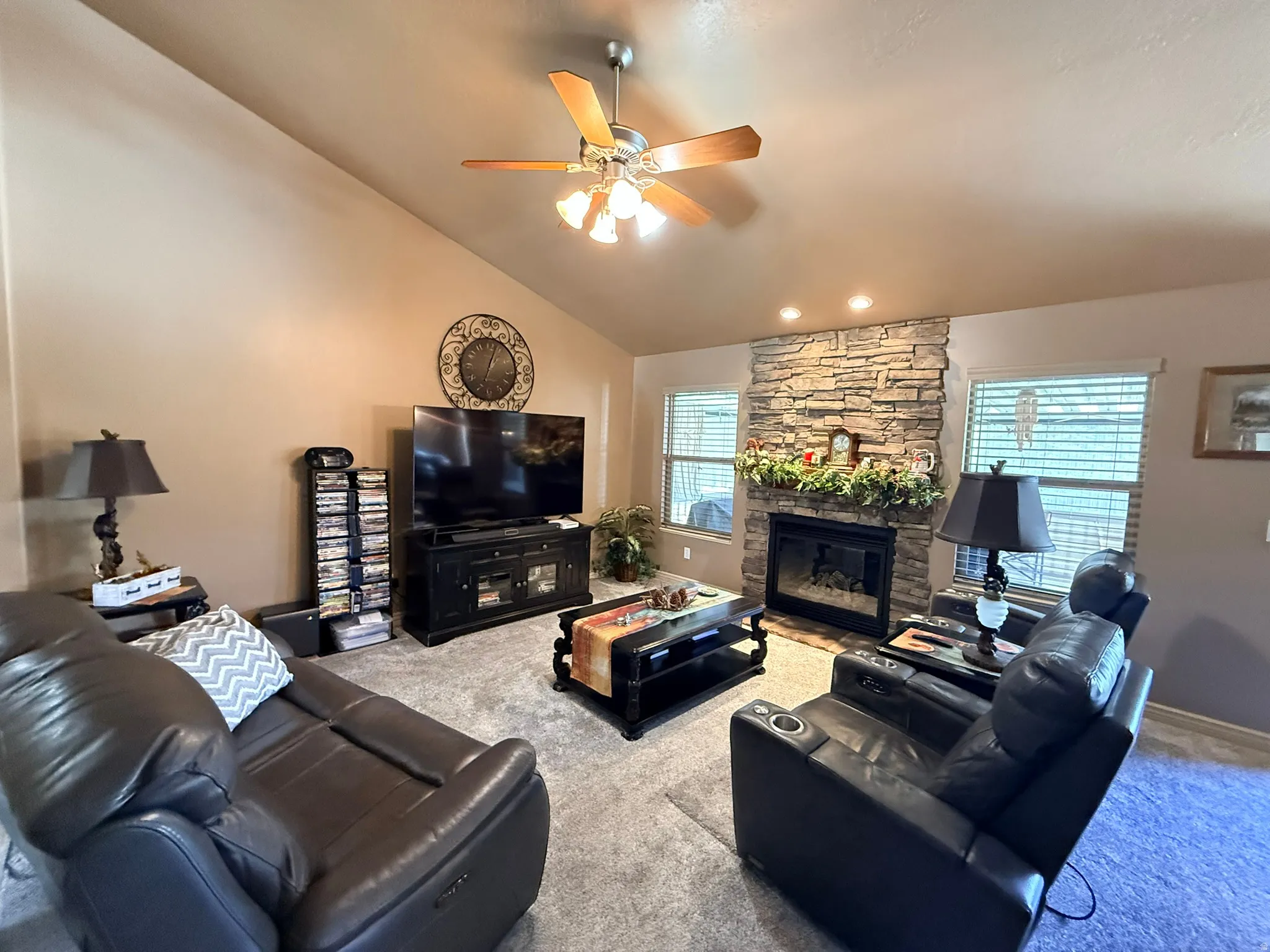 Living room featuring a stone-faced fireplace with a black insert, vaulted ceiling, and recessed lighting