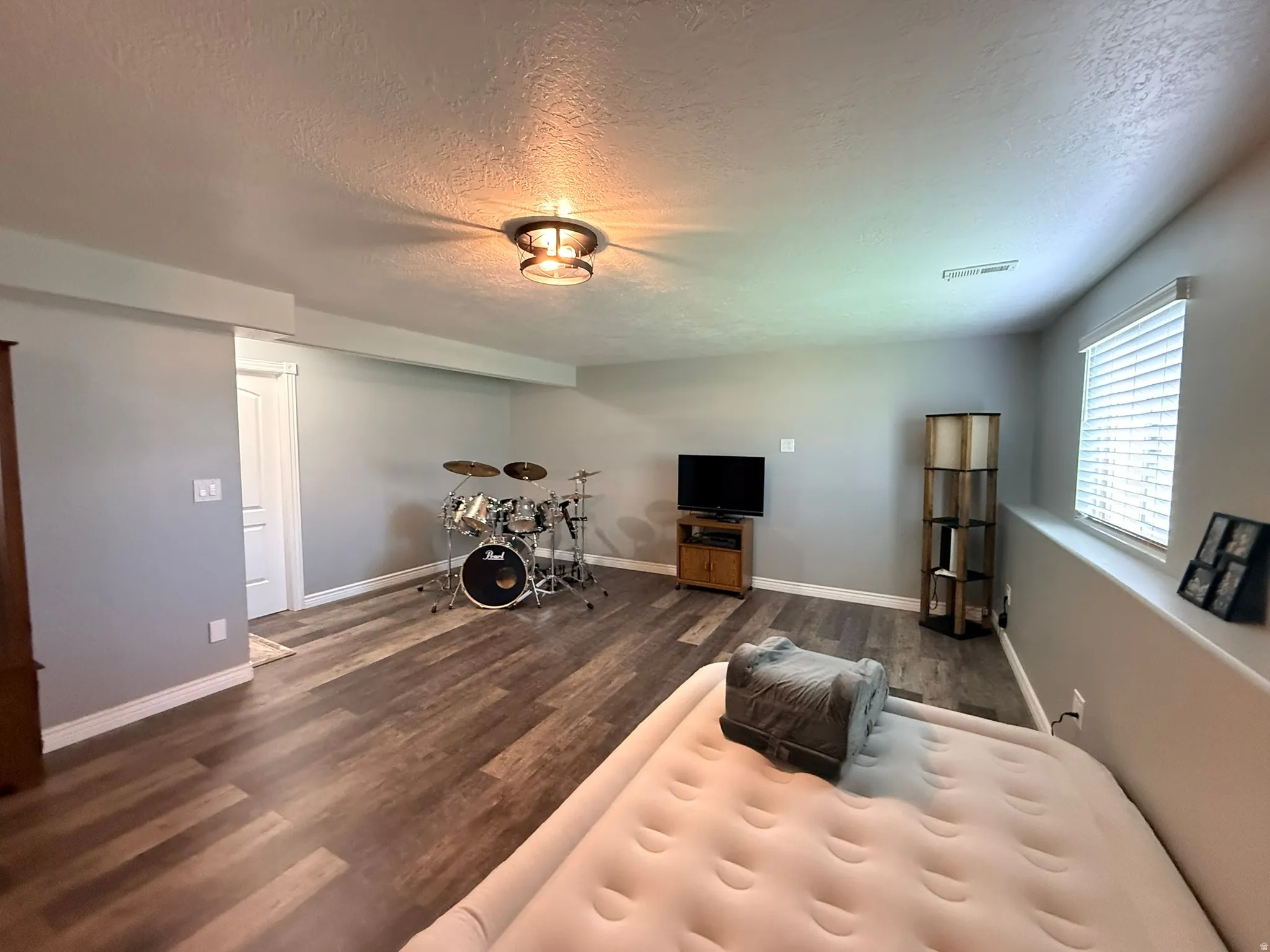 Spacious room featuring wood-finish flooring, light gray walls, and a recessed window with blinds