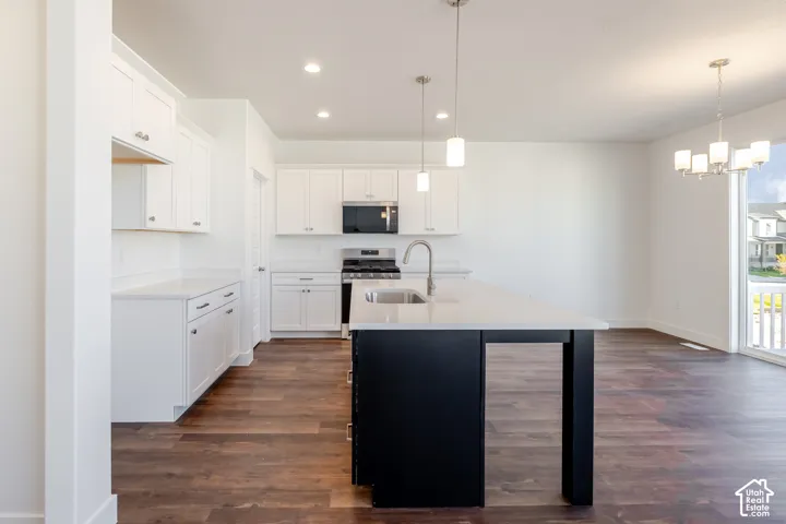 Kitchen featuring white cabinetry, a central island with a sink, stainless steel appliances, wood-finish flooring, and pendant lighting