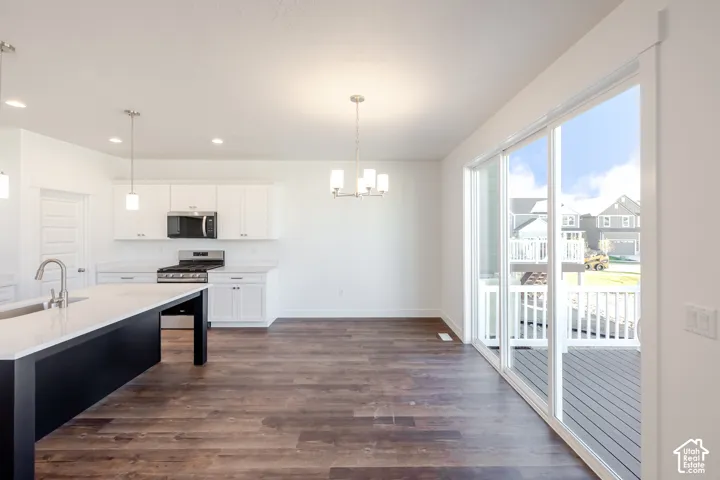 Kitchen with white cabinetry, stainless steel appliances, dark wood-finish flooring, and a large center island with light-colored countertop
