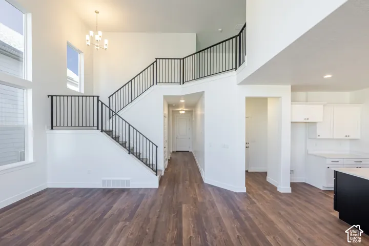 Two-story entryway featuring wood-finish flooring, a contemporary chandelier, a multi-level staircase with black iron railings, and multiple windows