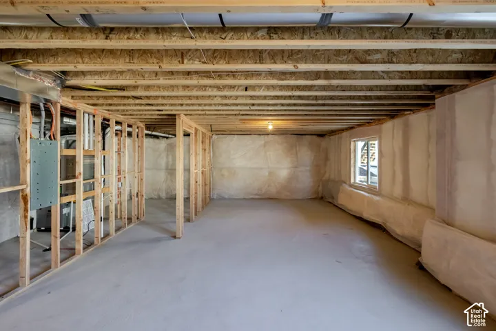 Unfinished basement featuring exposed wood framing, concrete flooring, perimeter insulation, an electrical panel, and a single window
