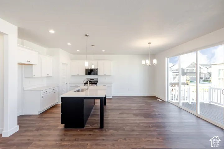 Open-concept kitchen featuring white cabinetry, a dark-toned island with an integrated sink, stainless steel appliances, and wood-finish flooring