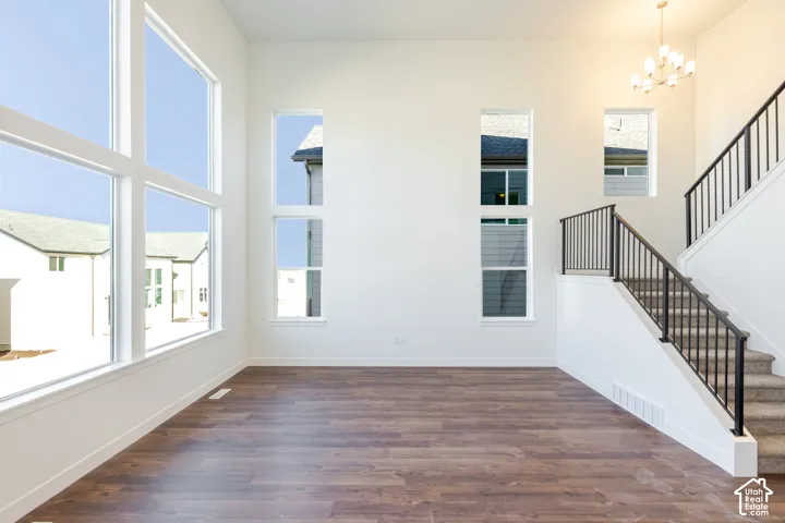 High ceilings with ample natural light, wood-finish flooring, staircase with carpeted treads and black metal railings, and a multi-arm chandelier