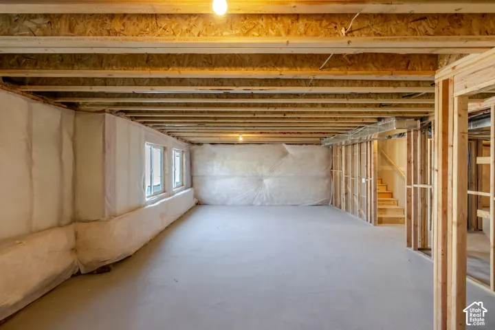Unfinished basement with exposed ceiling joists, three windows, and framed walls