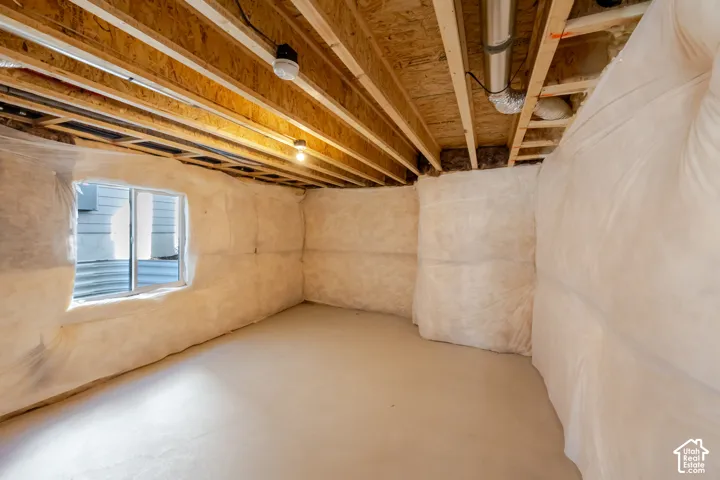 Unfinished basement space featuring exposed wood joists, a dedicated window opening, and insulated wall sections